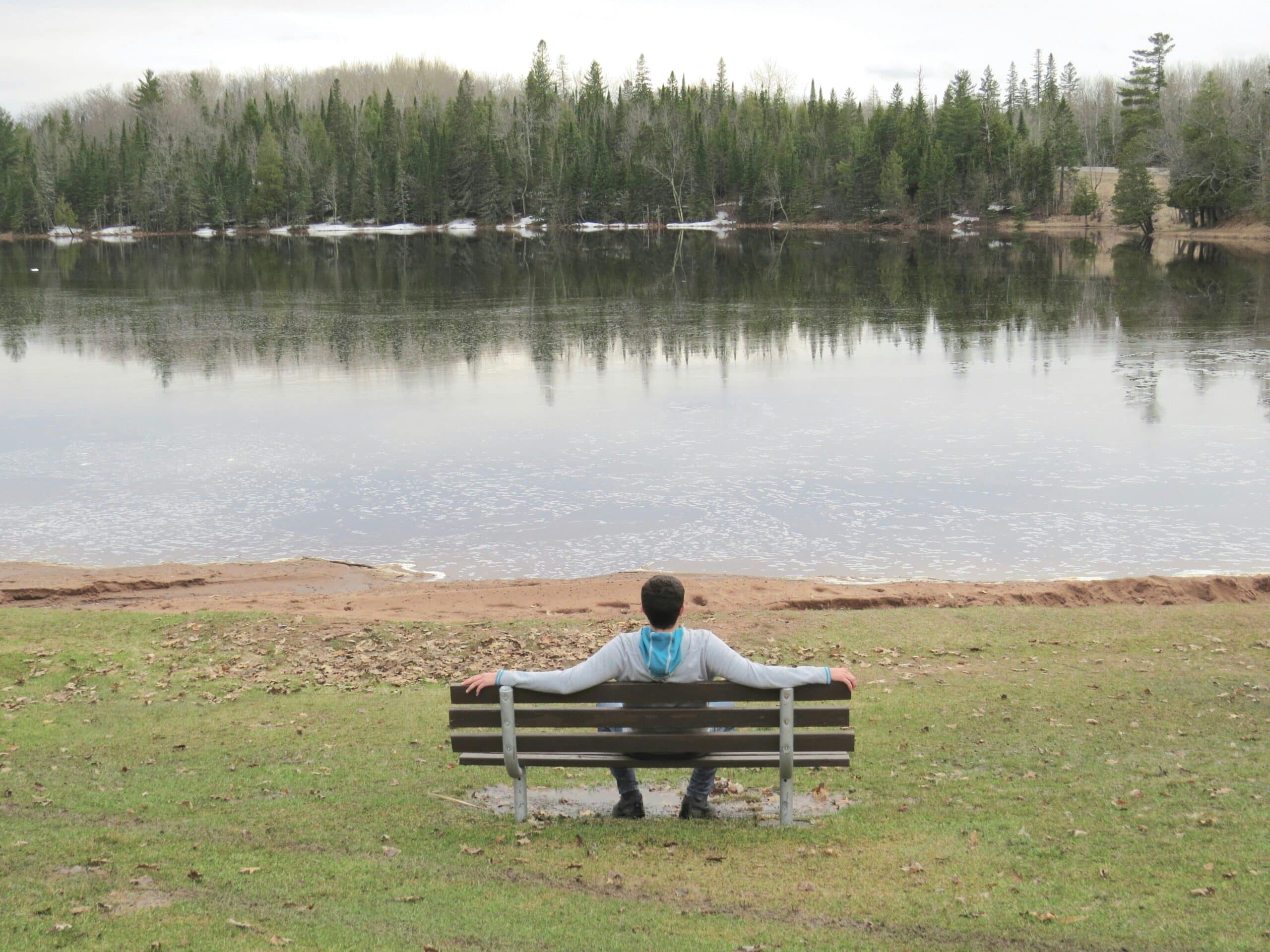 Person sitting on a bench by a lake, reflecting in a calm natural setting as part of the healing process