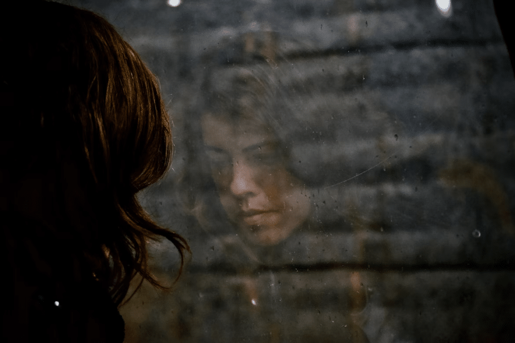 Person reflected in a window, representing inner reflection and emotional processing during trauma healing