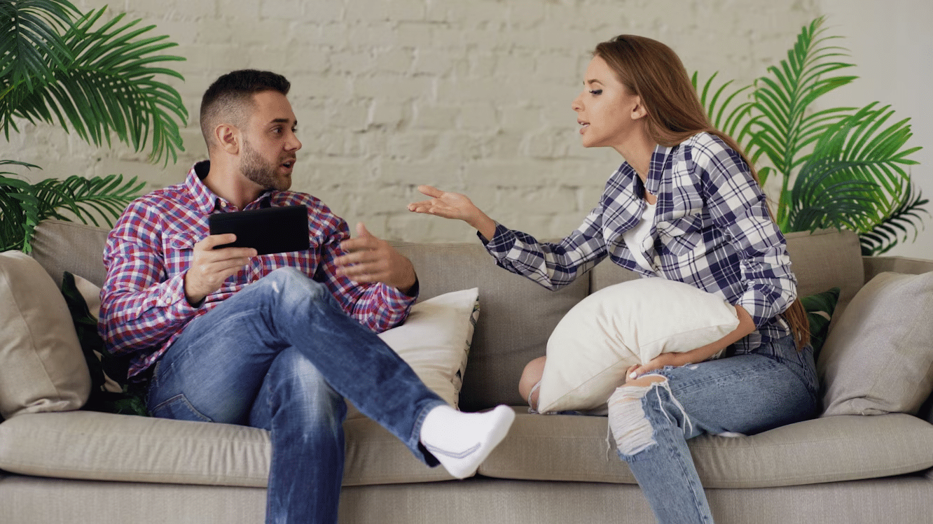 Couple sitting on a couch having a tense conversation, illustrating communication struggles in relationships